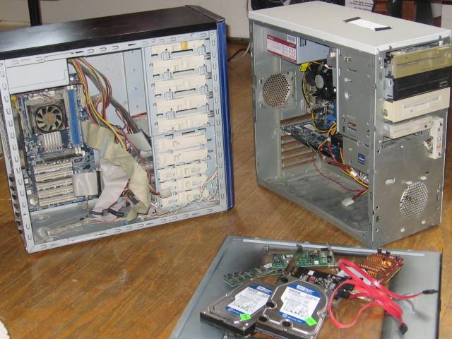 The two computers beside eachother and opened up. Several hard drives are sitting on one of the casing sides.