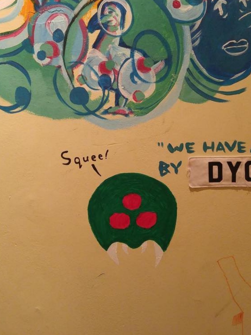 A closeup of the Metroid, playfully saying squee, upon the wall of the art house.