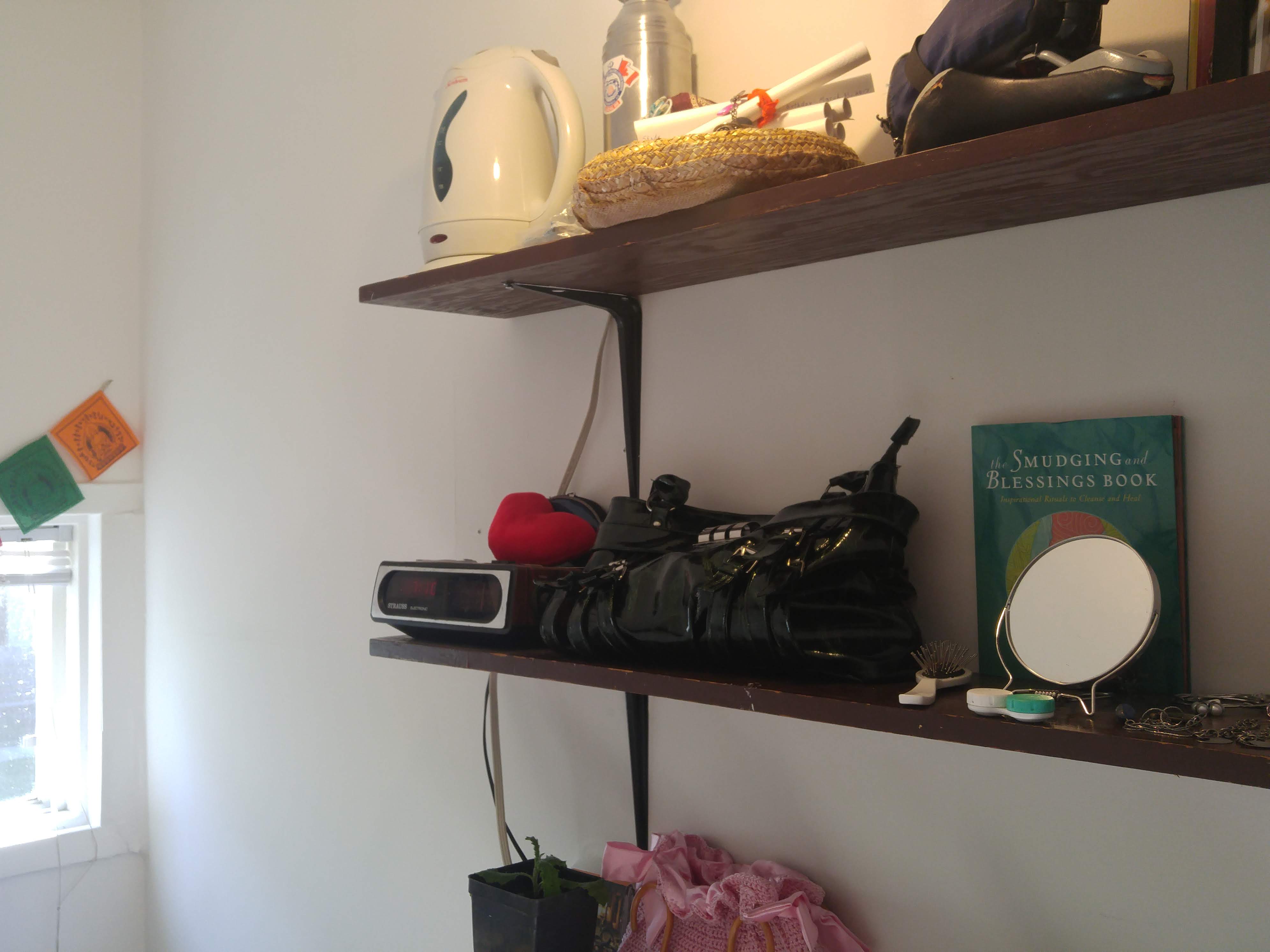 The shelving on the other wall, with a clock, mirror, some books, a purse, the nest for her dragons and their adoption scrolls, an electric tea kettle, and a bike seat.