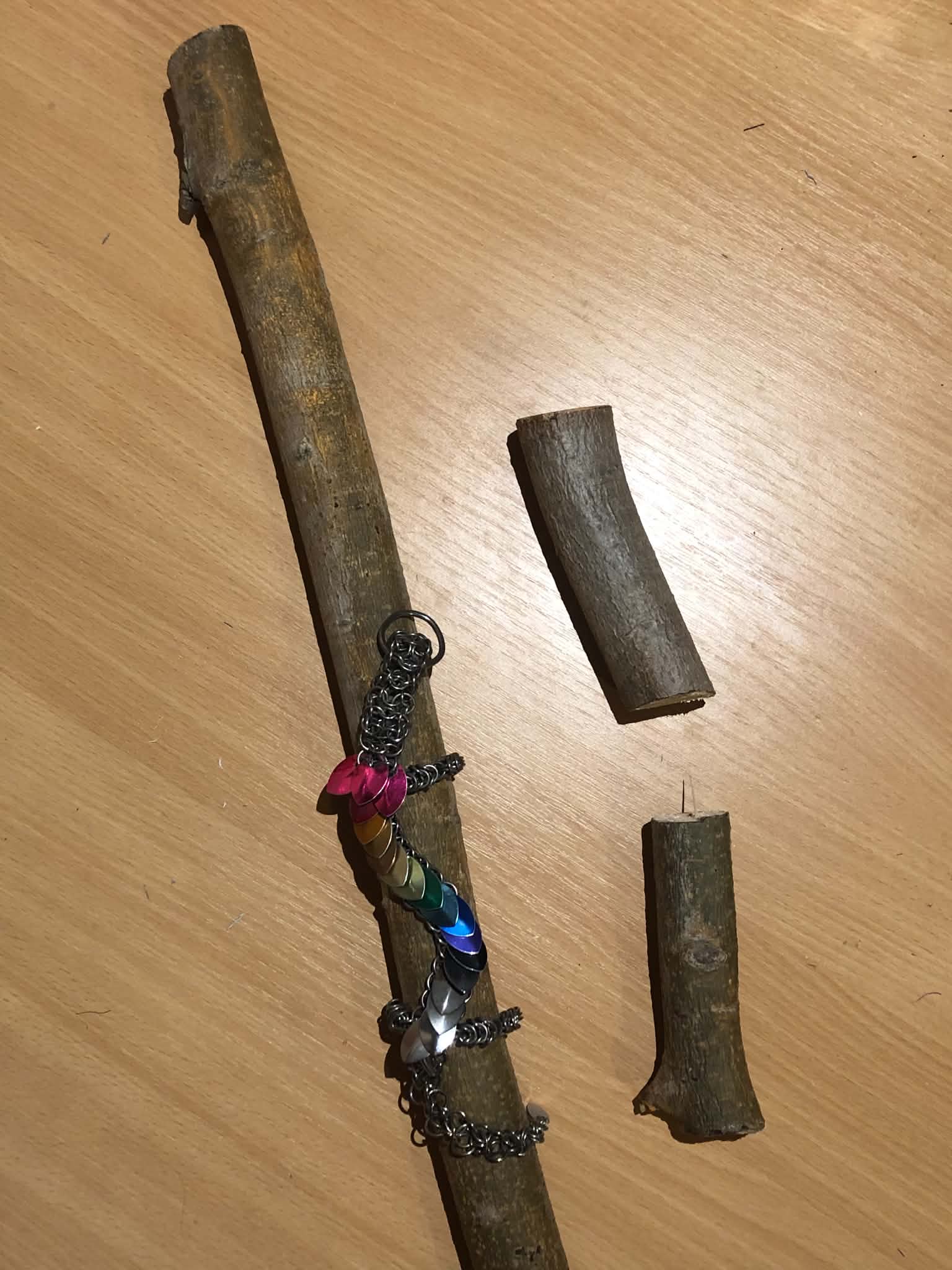 A poplar wood staff on a table, beside two pieces that were cut off to size it, and a colourful chainmaille dragon on top of it.