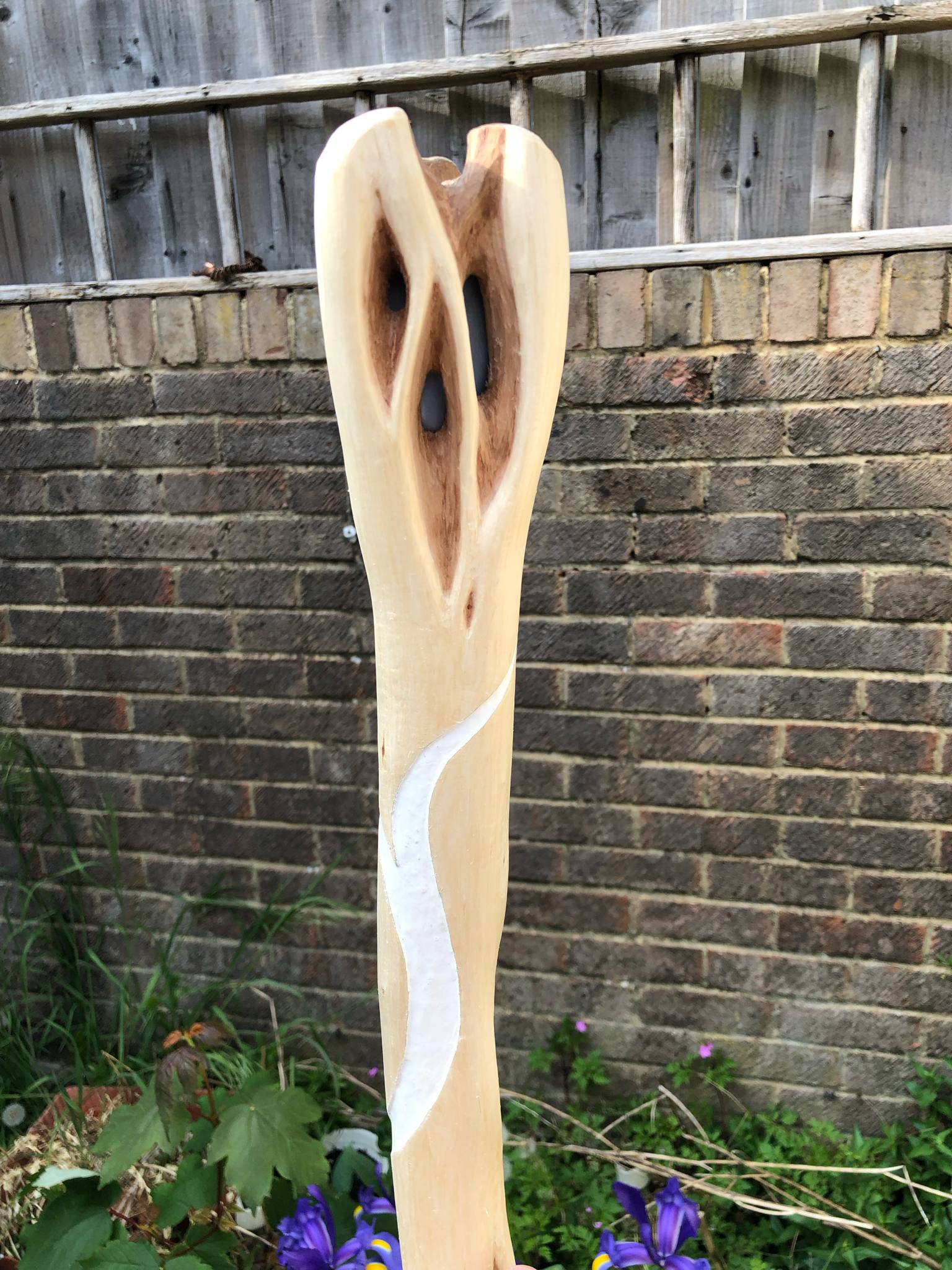A closer pic of the front of the head, looking somewhat like a face with two larger eyes open to the blue stone set inside, and one more eye below and between the other two. A carved white curve begins somewhat below the head and wraps around the staff.