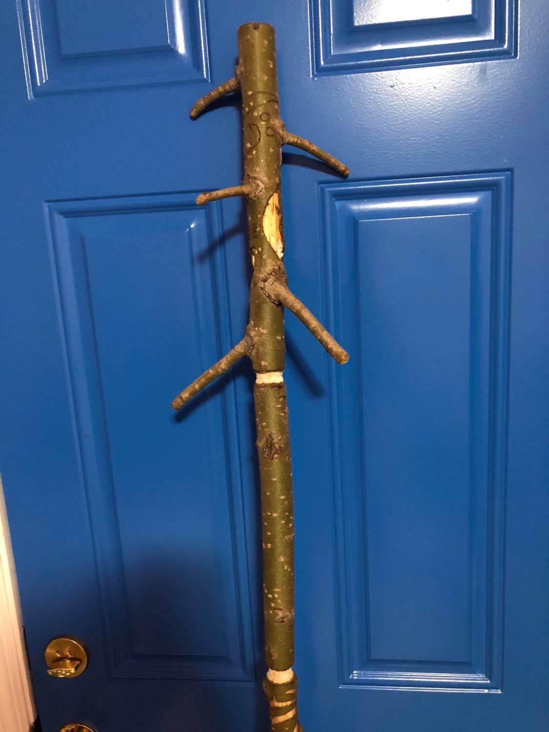 Showing the head of the staff with the long sticks poking out, beginning to have the faces carved into it.
