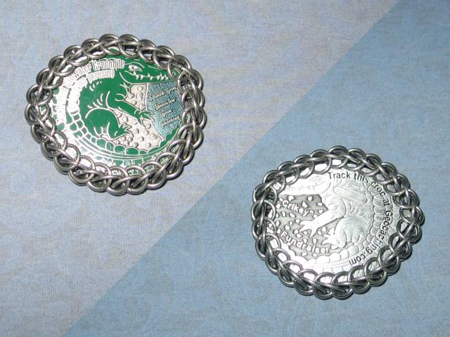 A split view of both sides of the coinf, on a light blue background. The one side is of a crocodile, while the other side shows where the tracking number would be, blurred out, and of course it is wrapped around the edge in chainmaille.