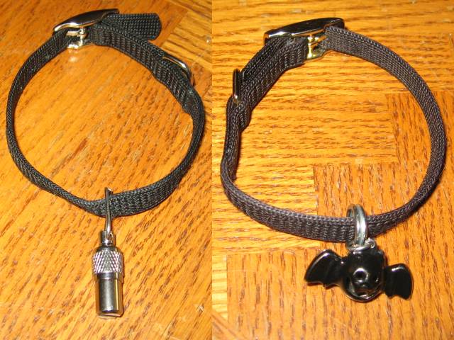 Two black nylon cat collars, one with a capsule tube beneath and one with a bell in the shape of a bat, shown on a wooden table.