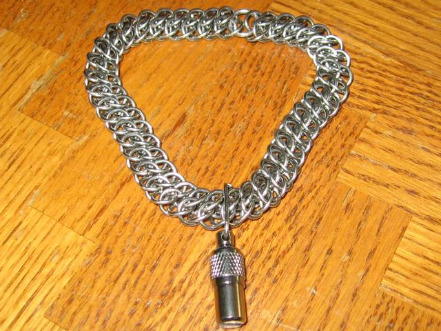 The first chainmaille weave, on a wooden table, and with the capsule attached.