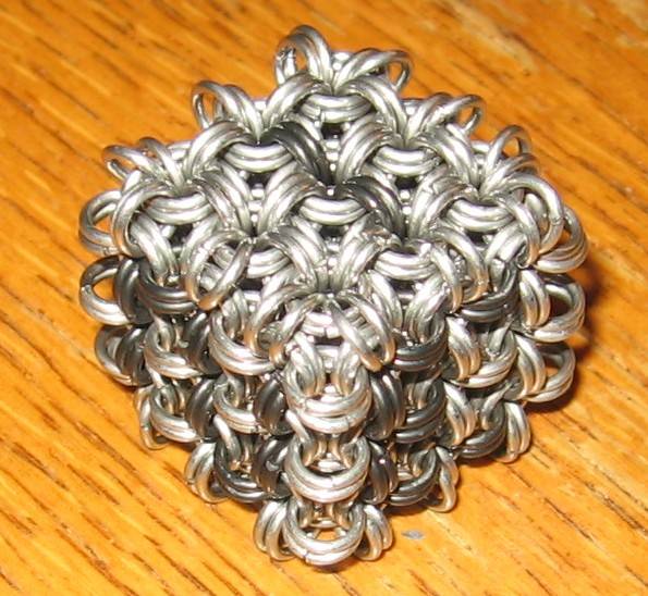 A closeup of the chainmaille dice, showing the numbers 1, 2, and 3, on a wooden surface.