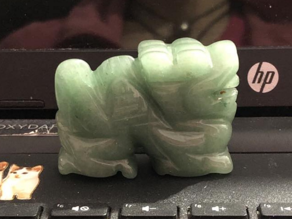 A green jade stone dragon sitting on a black laptop computer above the keys between a cat sticker and an hp symbol.
