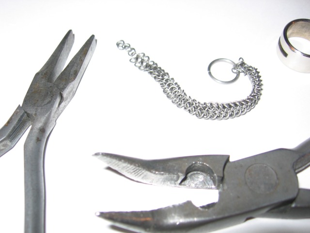 The ring about half-made, sitting beside the pliers being used to make it.