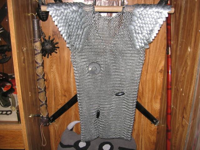 The chainmaille shirt hanging in a wooden display case, with magnets having been tossed onto it.