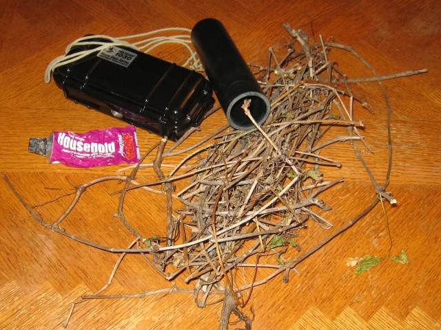 A pelican container and pvc pipe, some glue, and some twigs and roots on a table.