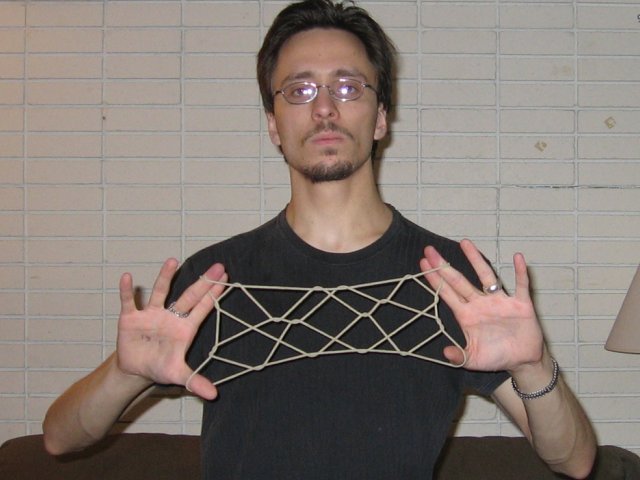 Kabutroid holding up the Many Stars string figure in front of a brick wall and brown couch, with a normal face for this one.