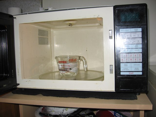 A measuring cup with water and strips of paper in it sitting inside of a microwave.