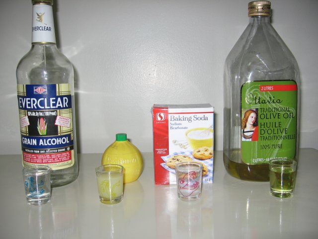 Everclear, lemon juice, baking soda, and olive oil, behind respective shotglasses of the fluids.