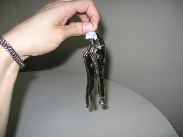 A piece of paper with a vice grip pliers clamped onto it and hanging from it.