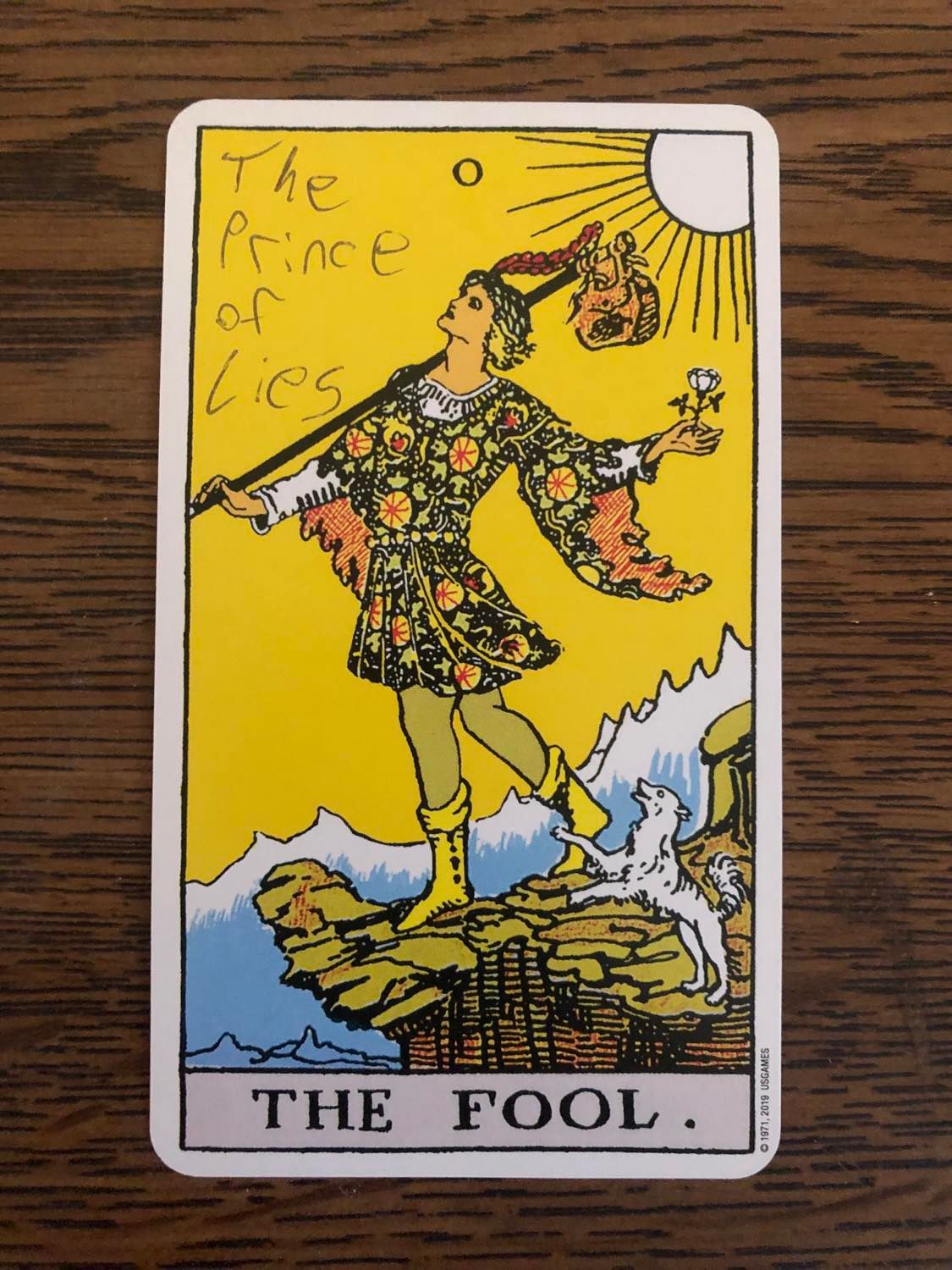 The fool card with the prince of lies written on it, laying on a wooden desk.