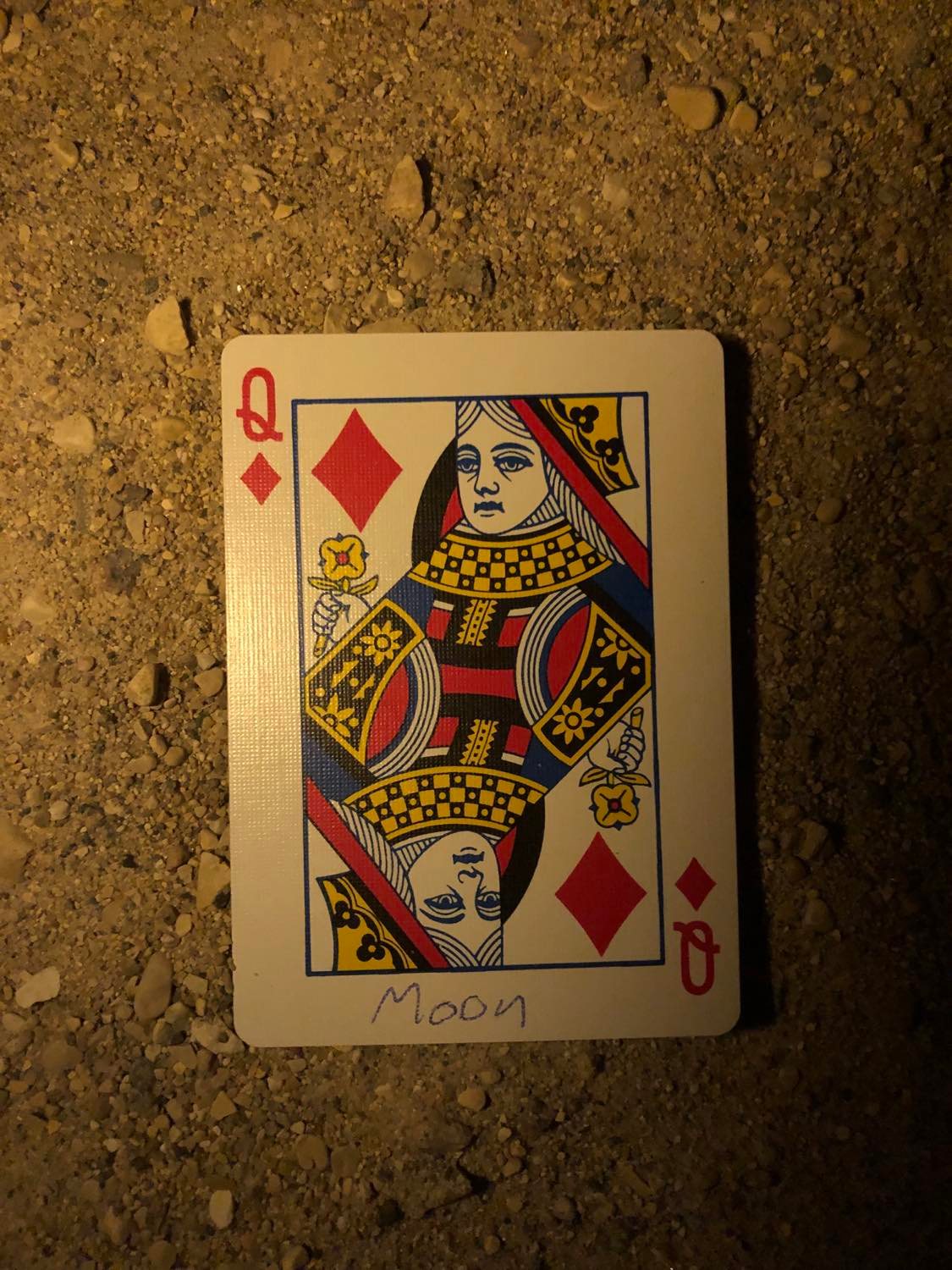 The queen of diamonds with Moon written on it, laying on the darkened soil.