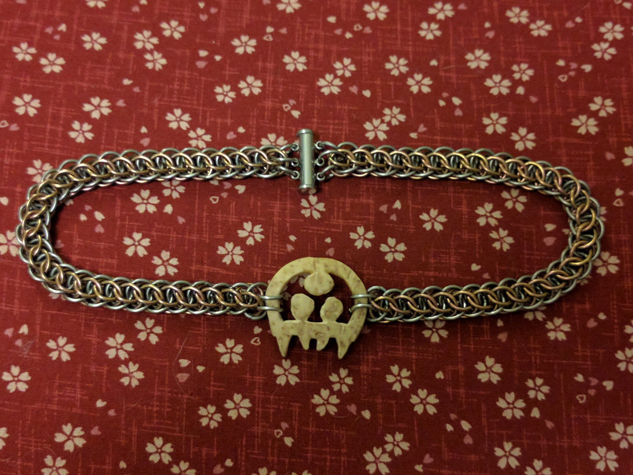 The Metroid pendant with the rounder chainmaille weave, now flatter looking on the burgundy surface, with a tube clasp.