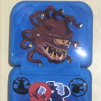 A tiny dice tower made from a tiny blue sewing kit case and clear plastic