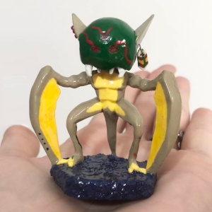A shiny painted Kabutroid figurine with the yellow scythe arms, green metroid head, earrings, and tattoos on a lumpy blue base, sitting on Kabutroid's hand.
