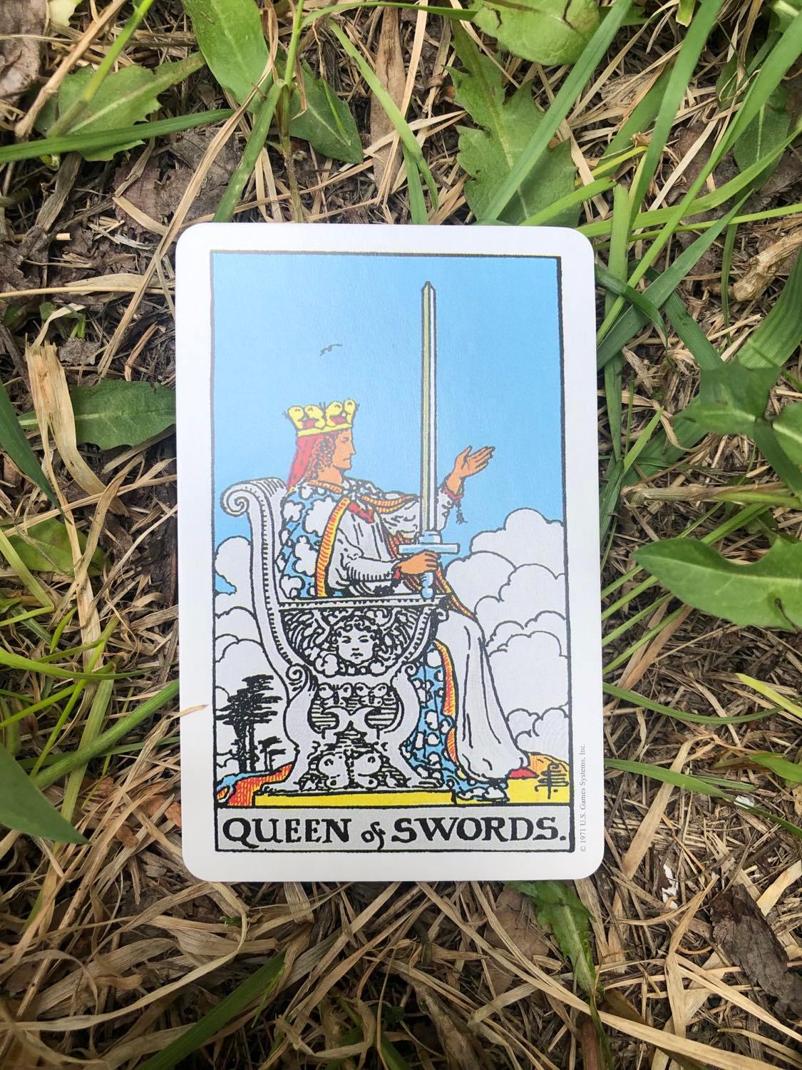 The Queen of Swords, upright, laying in the grass.