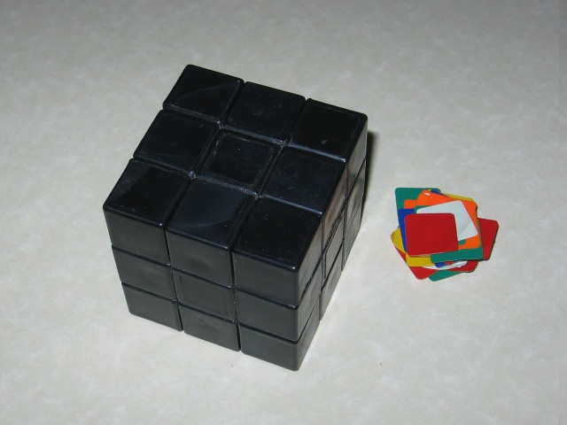 The Rubik's cube with all of the stickers peeled off and stuck together in a pile to the right.