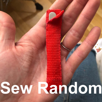 A small, thin red pouch made from a nylon strap, holding a pair of tweezers inside of it.