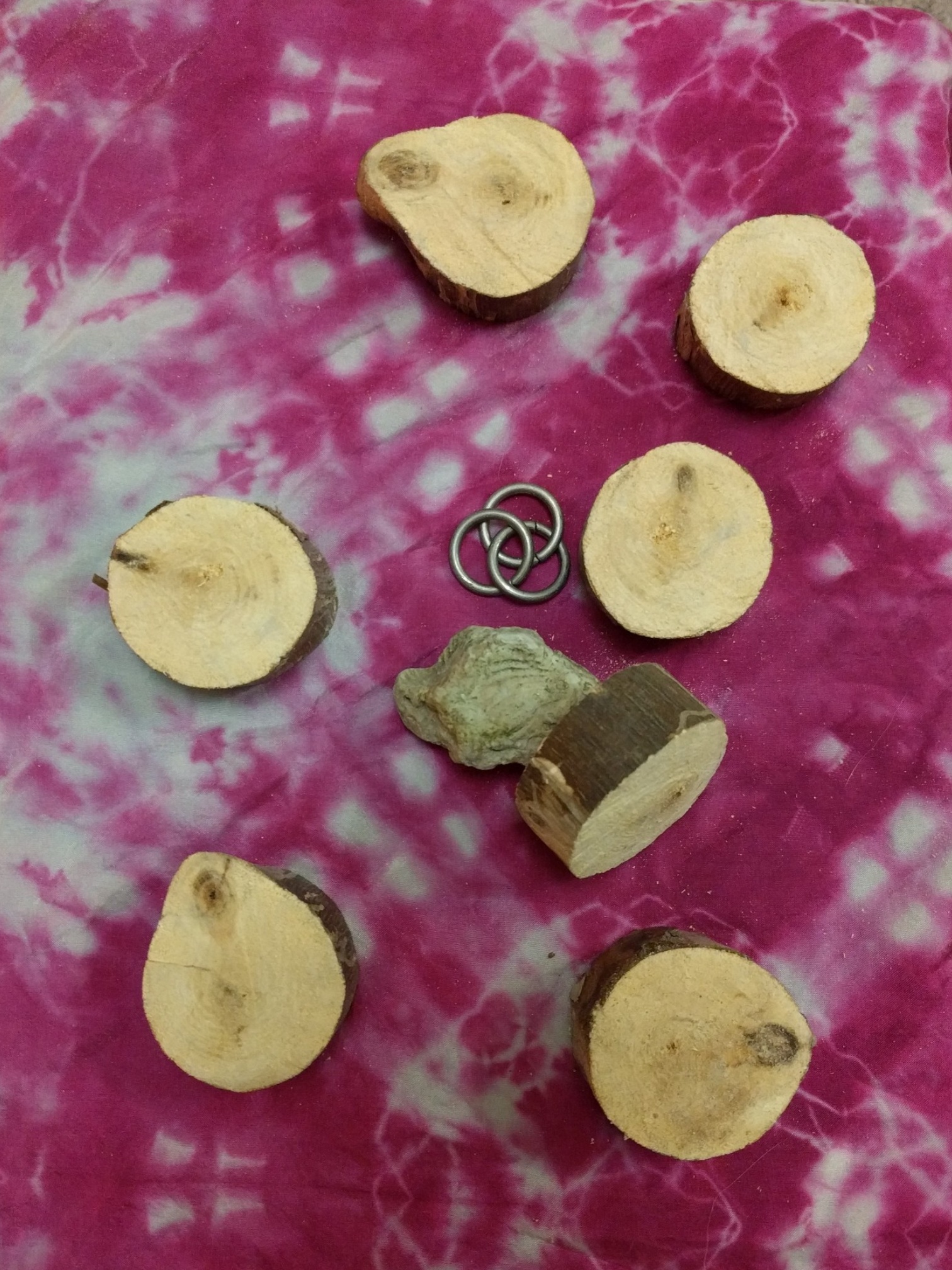 A set of seven wooden disks, a fossilized stone, and three metal rings, on a pink silk pattered cloth.