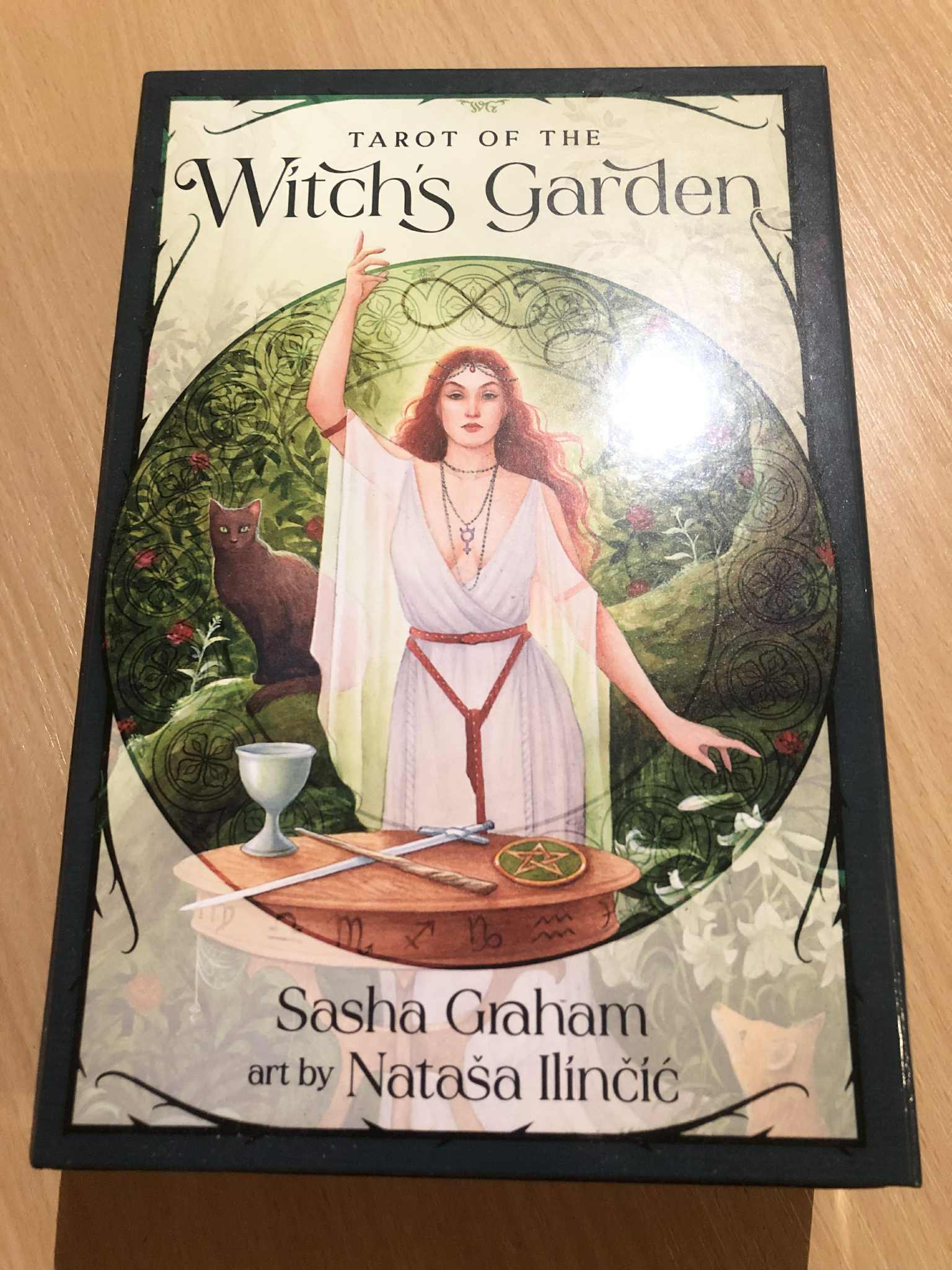 A tarot deck depicting a witch with a cat, surrounded by glowing white, standing in the woodlands with her hand up, and the four suits in front of her. The most friendly woodland deck that I know.