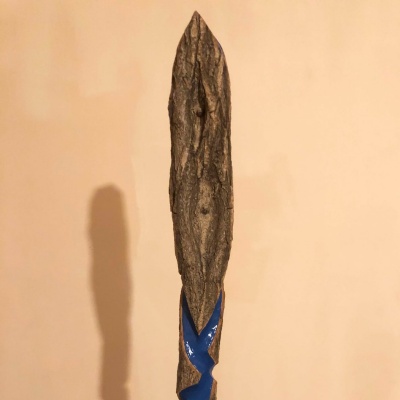 The head of a wooden staff that has the appearance of a large pair of eyes, with some carving beneath the head.