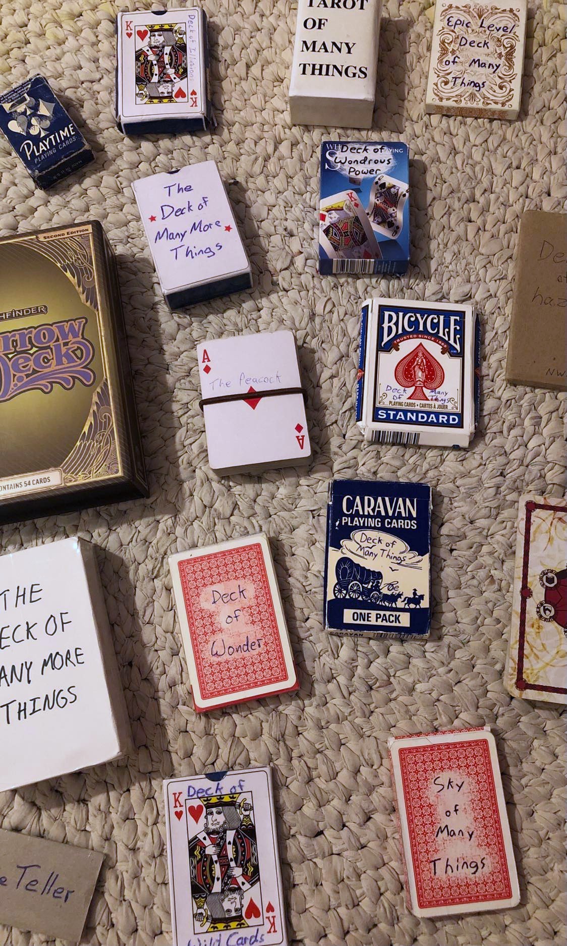 All of the various decks of many things, from the harrow deck to the deck of wondrous power to the sky of many things, multiple copies of some of them, all spread out on a white crocheted rug.