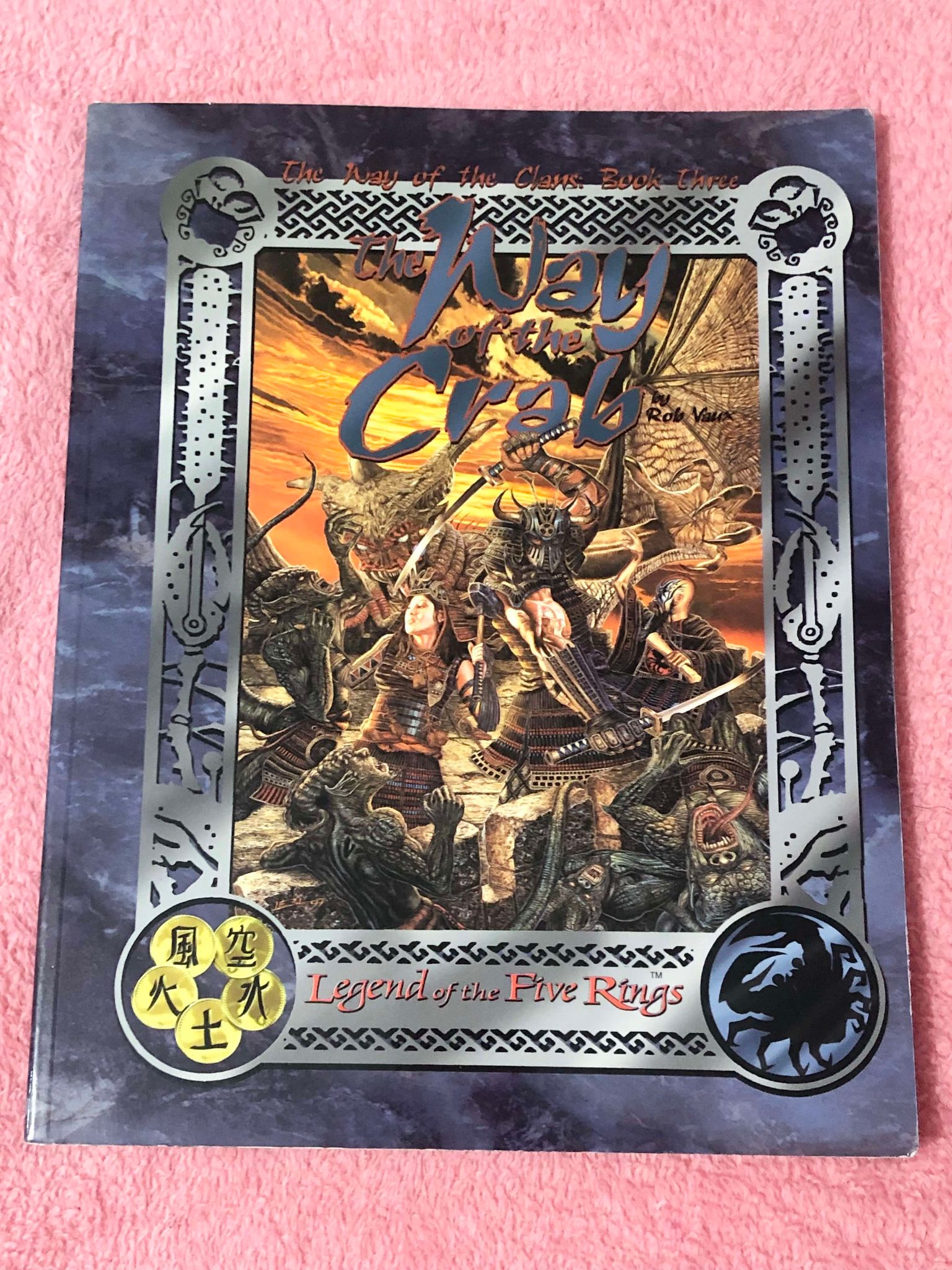 A blue book with orange sepia toned image in the center showing several bushi fighting an oni and other monsters. Way of the Crab, which has letters and details about the Crab clan and their way of life.