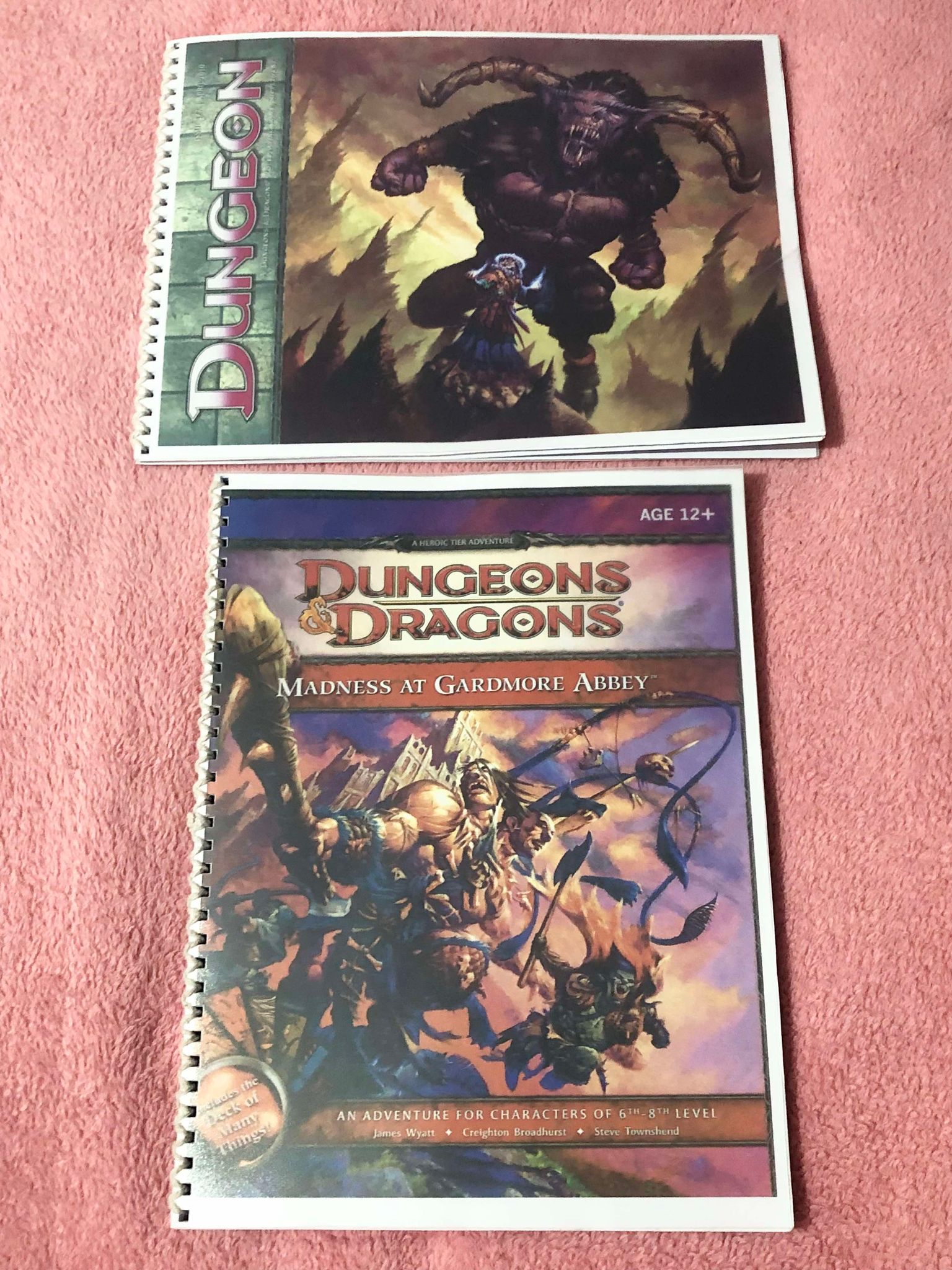 Two more bound books on a blanket, Dungeon magasine number 177 depicting a giant minotaur being led by a wizard, and Madness at Gardmore Abbey, a heroic tier adventure showing a two headed fighter with a spiked club and a goblin creature on the cover.