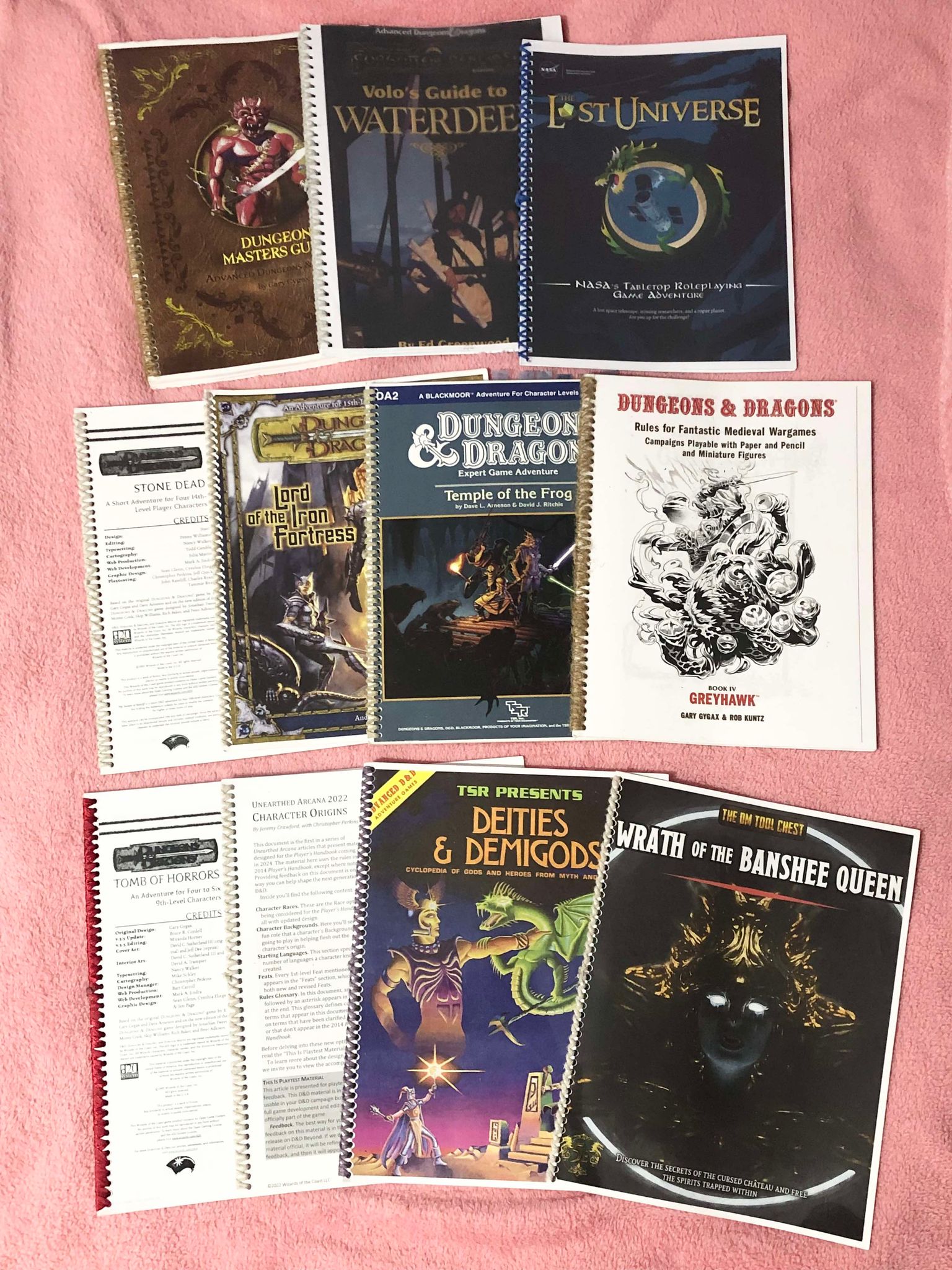 A pile of eleven printed and bound books and modules, such as Lord of the Iron Fortress, the first edition Dungeon Master's Guide, Wrath of the Banshee Queen, or the Unearthed Arcana 2022 when Wizards of the Coast were workshopping towards the new 2024 core rulebooks!