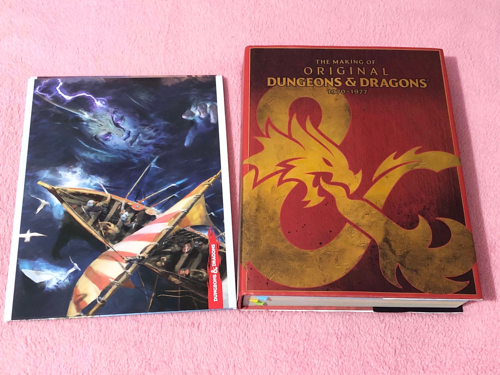 The DM screen showing the side that has a giant underwater reaching up towards a ship, sitting beside the giant red tome for the making of the original Dungeons and Dragons, an epic book with unreleased notes, letters, and full copies of the original Chainmail, Blackmoor, and Greyhawk books!