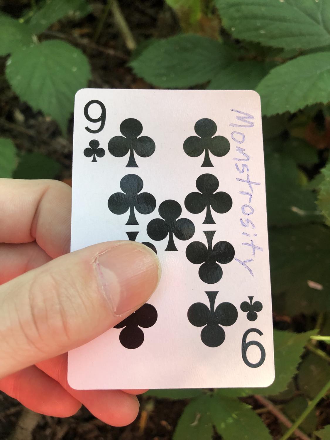 The nine of clubs with the word Monstrosity written on it, held above the brush.